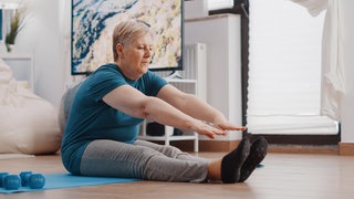 Frau sitzt auf Matte und macht eine Übung