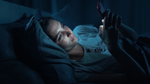 Frau liegt im Bett und schaut aufs Handy