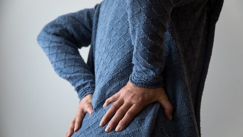 Eine Person hält sich den unteren Rücken wegen Kreuzschmerzen. Der neue IGeL-Monitor sieht die Wirksamkeit von Osteopathie gegen solche Beschwerden weiterhin als fraglich.