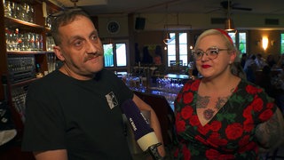 Matthias Oechsler ist Quizmaster in der Kneipe SchnickSchnack in Niederbühl. Gemeinsam mit einer Frau lehnt er am Tresen.
