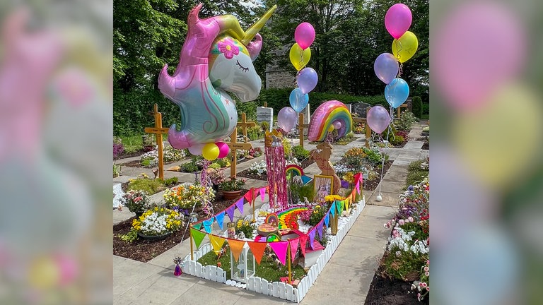 SWR1 Neuanfang: Bunt und fröhlich, so wie Lenya war - das Grab ist geschmückt mit farbigen Fähnchen und bunten Regenbogen-, Einhorn- und Helium-Ballons. Auch ein kleines Holzpferd fehlt nicht.
