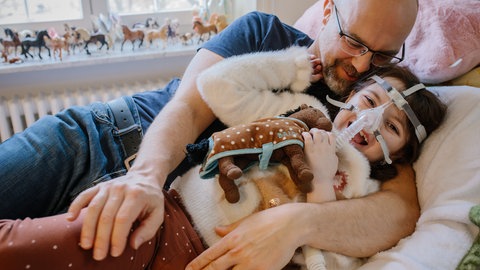 SWR1 Neuanfang: Lenya kuschelt mit Papa Arne im Krankenbett im Kinderhospiz Stuttgart. Durch ihre schwere Erkrankung – ein Gendefekt names CMS – verlor Lenya Stück für Stück jede Muskelkraft.