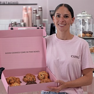 Michelle Mignogna hält eine Schachtel mit ihren Cookies in der Hand und schaut in die Kamera.