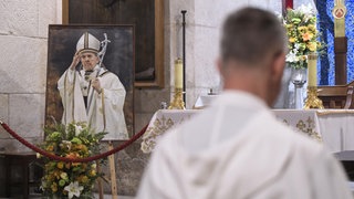 Ein Bild des verstorbenen Papstes Franziskus in einer Kirche | Tod von Papst Franziskus: Was jetzt im Vatikan passiert
