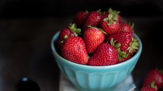 Erdbeeren liegen vor dunklem Hintergrund in einer blauen Porzellanschale. Wie kann man Erdbeeren konservieren?