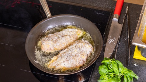 Die Geflügelbrust mit der Panade aus Parmesan wird in einer Pfanne angebraten.