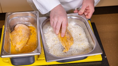 Die Panade aus Parmesan wird auf die Geflügelbrust aufgetragen