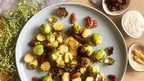 Rezept Rosenkohl aus dem Ofen mit Seelachs: Teller mit gebackenem Rosenkohl mit Nüssen, daneben drei kleine Schüsseln mit verschiedenen Dips 