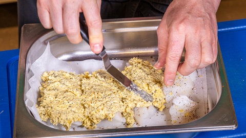 Fischfilet Bordelaise panieren: Der Fisch wird in einer Auflaufform mit der Panade bestrichen und fürs Backen im Ofen vorbereitet.