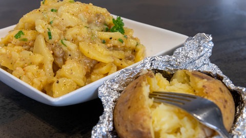 Karroffelsalat aus gegrillten Kartoffeln in ener Schale angerichtet und daneben ein Folien-Kartoffel frisch vom Grill.