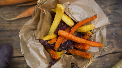 Pommes von Kartoffeln und Süßkartoffeln liegen fertig gegart in zerknülltem Pergamantpapier