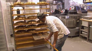 Ein Bäcker legt Brotlaibe in ein Regal