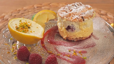 Vanille-Wolken-Törtchen mit Himbeersoße und gefüllte Zitronen auf einem bezuckerten Teller