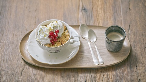 Rhabarber-Beeren-Crumble mit Pistazieneis stehen neben einem Kaffee auf einem Tablett