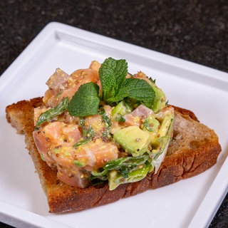 Rezept für Lachstatar mit Avocado: Das fertige Gericht ist auf geröstetem Brot angerichtet.
