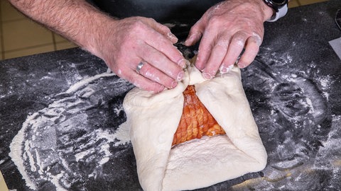 Der Braten wird auf einer mehrbestäubten Arbeitsplatte in Hefeteig gewickelt: Für den Kassler im Brotteig wird das Fleisch em Rezept von SWR4 Konditor Joachim Habiger zufolge im ausgerollten Teig versteckt.