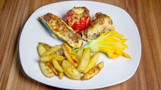 Gefüllte Zucchini mit Ofenkartoffeln und Gartendip auf einem Teller