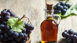 Flasche mit Essig, daneben steht ein Korb mit Trauben
