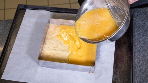 Ein Konditor gießt die Füllung für einen Zitronenkuchen, bzw. Zitronenecken auf einen Teig in einer Form. 