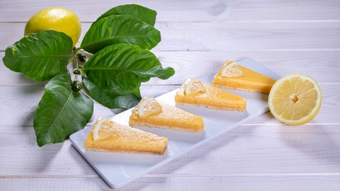 Sommerkuchen: Erfrischender Zitronenkuchen in Form von Zitronenecken auf einem rechteckigen Teller arrangiert mit einer Zitrone und einem grünen Zweig.