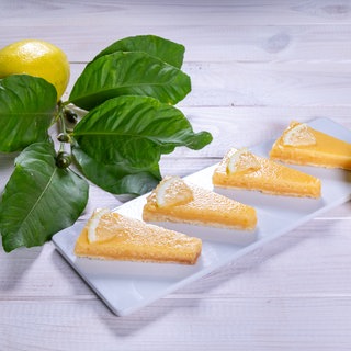 Sommerkuchen: Erfrischender Zitronenkuchen in Form von Zitronenecken auf einem rechteckigen Teller arrangiert mit einer Zitrone und einem grünen Zweig.