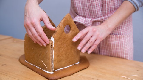 Eine Frau klebt ein Lebkuchenhaus mit Zuckerguss zusammen