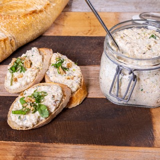 Aufstrich aus Gemüse, Hirse und Frischkäse ist in einem Glasgefäß und lecker angerichtet auf einem Baguette.