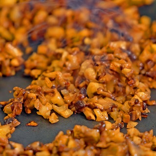 In einer Pfanne sind kleingehackte Pilze und Walnüsse, aus denen veganes Hack gemacht wird. Eine Alternative zu Fleisch für Bolognese und andere Saucen.