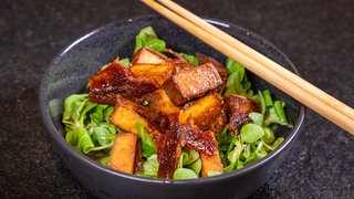 Gebackener Tofu auf Salat ist in einer kleinen Schüssel mit Essstäbchen angerichtet.