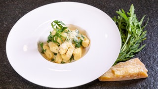 Vegetarisches Rezept für italienische Gnocchi mit Parmesanschaum und Rucola: Das Gericht ist auf einem weißen Teller angerichtet.