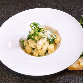 Vegetarisches Rezept für italienische Gnocchi mit Parmesanschaum und Rucola: Das Gericht ist auf einem weißen Teller angerichtet.
