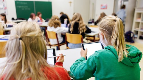 Schülerinnen einer sechsten Klasse arbeiten während einer Unterrichtsstunde an ihren Tablets. Ein Smartphone-Verbot an Schulen ist wissenschaftlich sinnvoll, im Unterricht soll nur mit Schulgeräten gearbeitet werden.