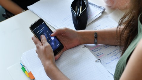  Eine Schülerin hält im Unterricht ein Smartphone in den Händen. Was sagt die Wissenschaft zum Smartphone-Verbote an Schulen?