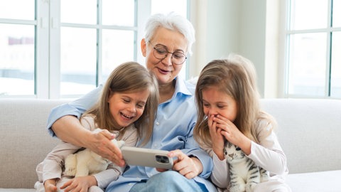 Frau und zwei kleine Mädchen schauen in ein Smartphone. Smartphones Kinder Gefahren