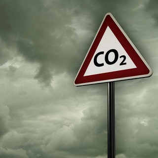 CO2-Warnschild vor grauen Wolken: Der Treibhauseffekt beginnt teilweise schon unmittelbar über der Erdoberfläche, indem einfach Gase wie CO2, Methan und Wasserdampf die Wärmestrahlung von der Erde absorbieren und einen Teil diese Wärme wieder zurück zur Erdoberfläche abstrahlen. Um diesen Effekt zu entfalten, müsste das CO2 gar nicht in die Höhe aufsteigen. Trotzdem gelangt es in die obere Atmosphäre und dort entfaltet es eine zusätzliche Wirkung.