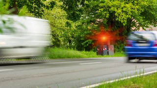 Zwei Autos fahren an Blitzer vorbei, der auslöst.