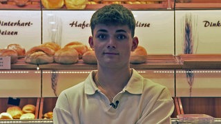 Linus Baur steht in einer Bäckerei. Er hat die Brötchenrutsche erfunden.