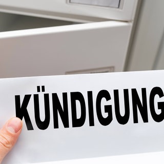 Eine Hand hält ein Kündigungsschreiben mit Aufschrift Kündigung vor einem geöffneten Briefkasten, symbolisch für den Verlust des Arbeitsplatzes.