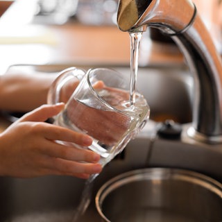 Wasser wird aus einem Hahn in eine Tasse gezapft