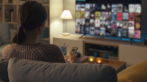 Frau sitzt auf der Couch und durchsucht die Mediathek