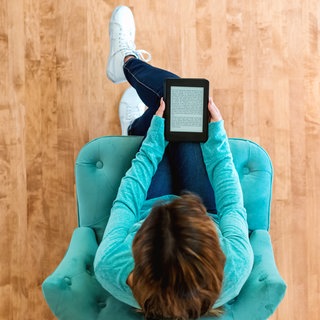 Frau sitzt im Sessel und liest in einem E-Reader