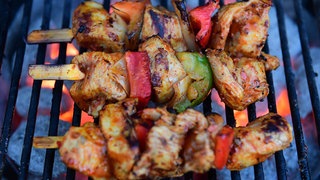 Fleischspieße liegen auf einem Holzkohle-Grill.