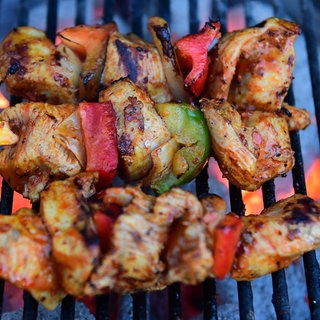 Fleischspieße liegen auf einem Holzkohle-Grill.