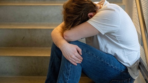 Ein Jugendlicher sitzt auf einer Treppe, den Kopf auf die Unterarme gelegt, sinnbildlich für Depression und psychische Probleme von Jugendlichen heute.