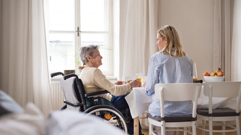 Ältere Frau im Rollstuhl und eine jüngere Frau sitzen am Tisch