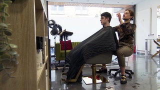 Friseur Dennis Boloban aus Karlsruhe ist Hair-Influencer. Er sitzt im Friseursalon und schneidet einem Kunden die Haare.