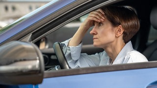 Ärger und Stress im Auto wegen Stau: Eine Autofahrerin stützt ihren Kopf auf die Hand und ist genervt vom Verkehr.