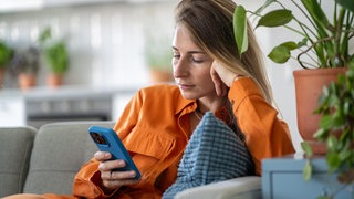 Warum wir Stress durch zu viele Verabredungen haben und was dagegen hilft | Eine junge Frau scrollt gestresst durch ihre Nachrichten in ihrem Smartphone