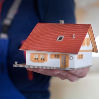 Symbolbild: Ein Handwerker hält ein Modell von einem Haus. | Die eigene Wohnung oder das eigene Haus kann durch einen Umbau altersgerecht werden.