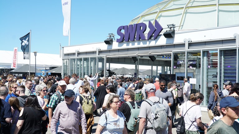 Bei sonnigem Wetter sind besonders viele Menschen auf dem Maimarkt unterwegs und schauen sich das Bühnenprogramm im Gläsernen Studio des SWR an.